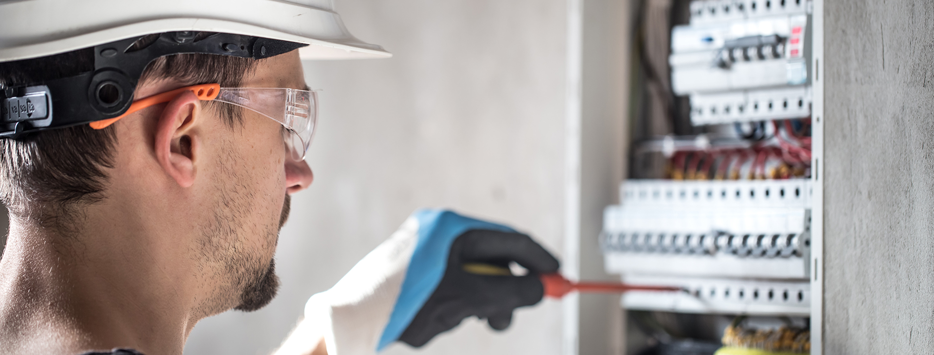 Elektroinstallateur mit Helm und Schutzbrille prüft Sicherungskasten an der Wand
