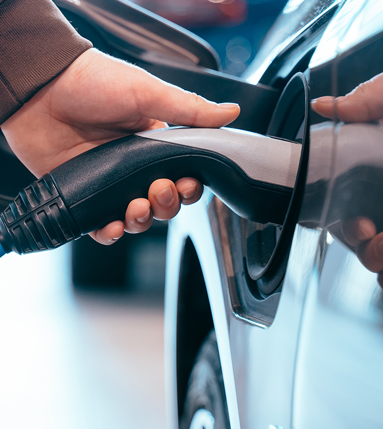 Eine Hand steckt einen Stecker in das Ladegerät eines Elektroautos.