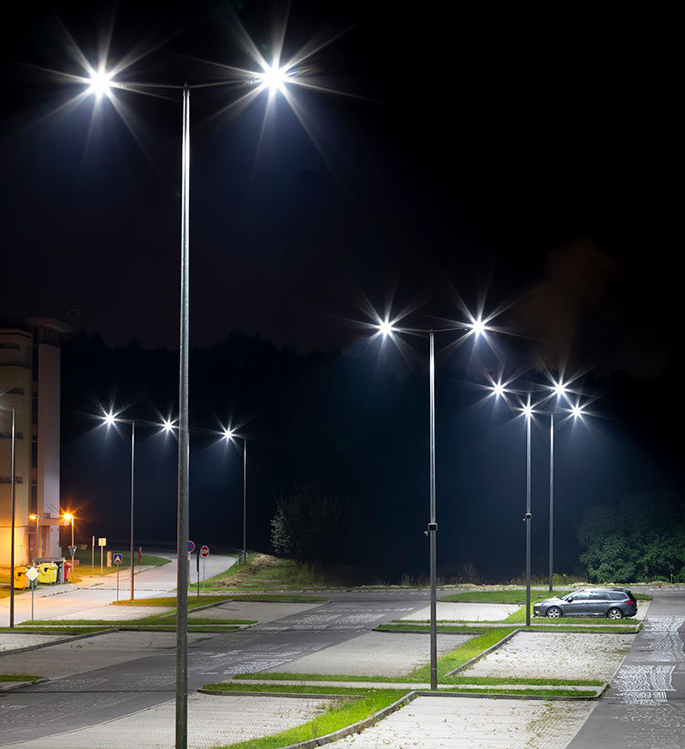 Straßenlaternen, die einen Parkplatz und eine Straße in Bochum in der Nacht beleuchten.
