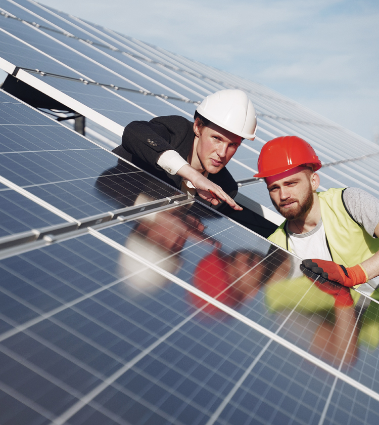 Zwei Männer mit Schutzhelmen überprüfen eine Solaranlage auf einem Dach.