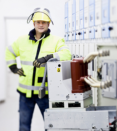 Ein Mitarbeiter in gelber Schutzkleidung und Helm steht vor elektrischen Schaltanlagen.